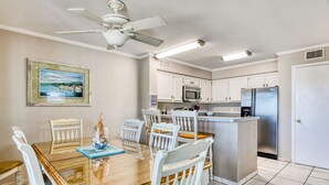 A kitchen with white cabinets, a stainless steel refrigerator, a microwave, and a dining table with white chairs. - Compass Rose 11, three-bedroom, two-bath condo, ocean front (Garden City Beach)