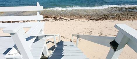 A wooden staircase leading to beach chairs on a sandy beach with the ocean in the background.