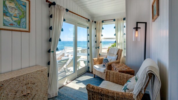 A cozy room with a view of the beach, featuring wicker furniture, a map on the wall, and a ceiling light. - High Hopes: Charming Oceanfront Cottage on the North End of Elbow Cay (Elbow Cay)