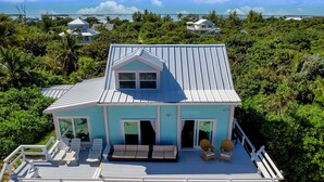 A light blue house with a white roof, a covered deck with white railings, and a view of the ocean. - High Hopes: Charming Oceanfront Cottage on the North End of Elbow Cay (Elbow Cay)