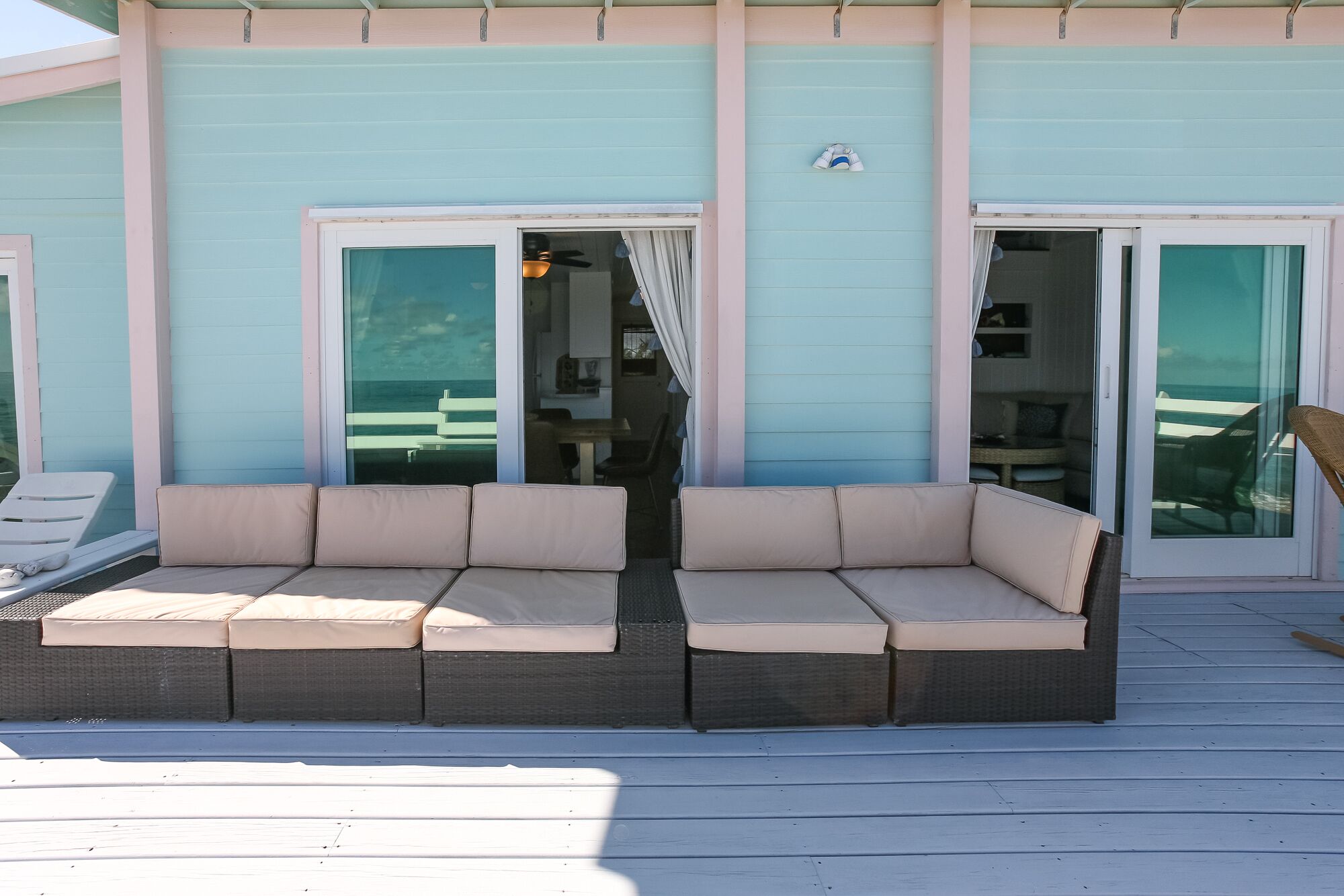 Un espace extérieur abrité avec des sièges, comprenant un banc rembourré et une table, une porte-fenêtre coulissante et un petit patio couvert.