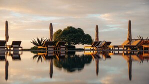 A serene pool area with lounge chairs and umbrellas, surrounded by a calm water body reflecting the sky.