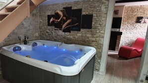 A hot tub in a room with stone walls and a wooden staircase.