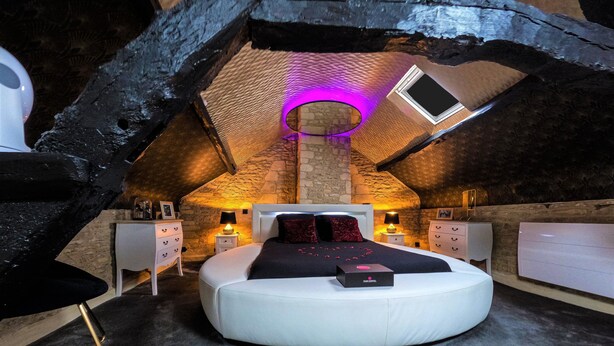 A circular bed in a rustic attic bedroom with stone walls, a skylight, and two bedside tables with lamps.