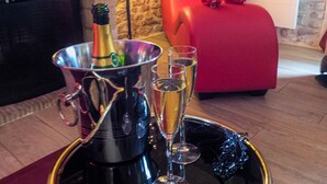 A tray with a champagne bottle and glasses on a reflective surface, a red chair, and a stone wall with a fireplace.