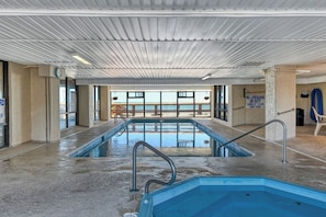 An indoor swimming pool with a view of a building outside, a lifeguard sign, and a no lifeguard on duty sign.