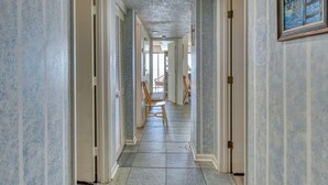Um corredor com piso ladrilhado, cadeiras de madeira e portas em ambos os lados.
