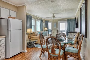 A spacious living area with a dining table surrounded by wicker chairs, a sofa, and a ceiling fan.