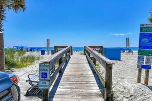 A wooden boardwalk leading to a beach with a sign indicating reserved parking and van accessibility.