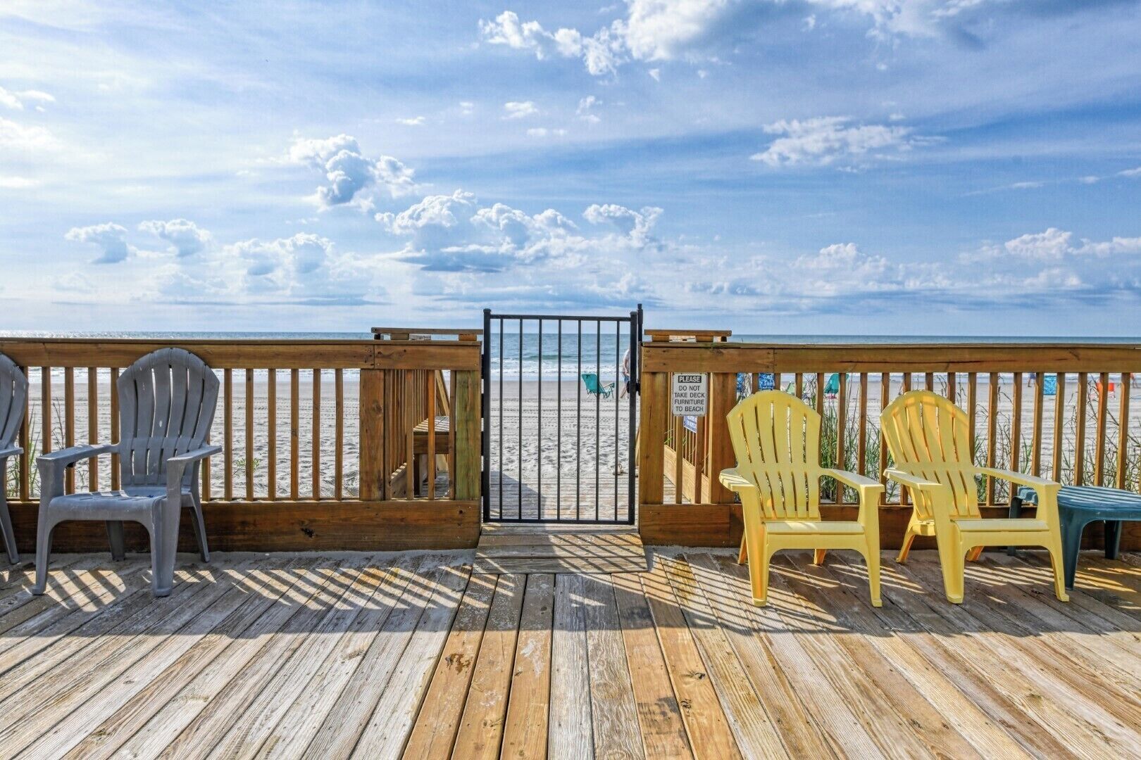 A wooden deck with chairs and a table, overlooking a beach with a clear sky.