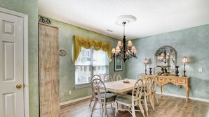 A dining area with a wooden table and chairs, a chandelier, and a dresser with a mirror. - Better Twin - Five Bedroom, Four 1.5 Bath Beach House with Ocean Views (Surfside Beach)