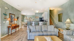 A spacious living room with a striped sofa, a wooden coffee table, and a dining area with a chandelier. - Better Twin - Five Bedroom, Four 1.5 Bath Beach House with Ocean Views (Surfside Beach)