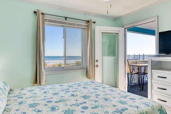 A bedroom with a bed, a window with curtains, a door leading to a balcony, and a TV on a dresser.