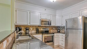 A kitchen with white cabinets, stainless steel appliances, a granite countertop, and a tiled backsplash. - Beach House 110, two-bedroom, two-bath ocean-view condo (Garden City Beach)