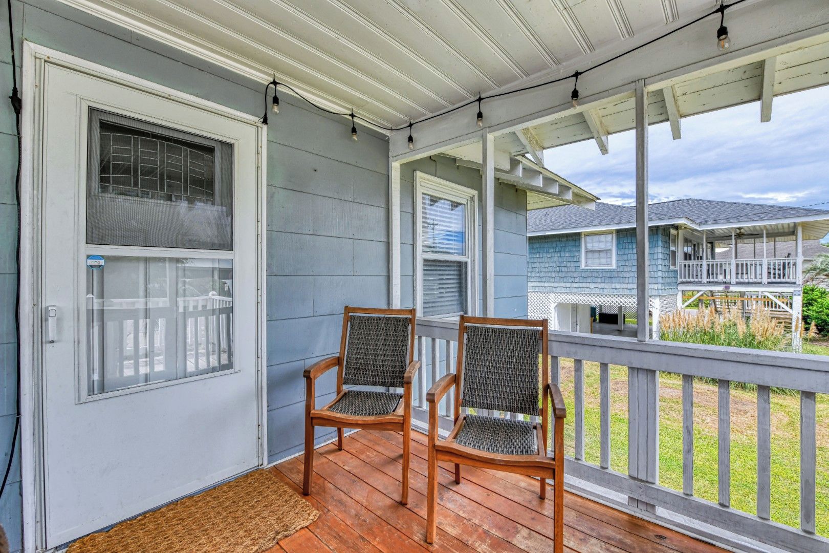 A porch with two wooden chairs, a wooden floor, and a view of a neighboring house.