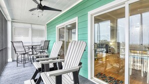 Eine überdachte Terrasse mit Adirondack-Stühlen, einem Tisch und einem Deckenventilator.