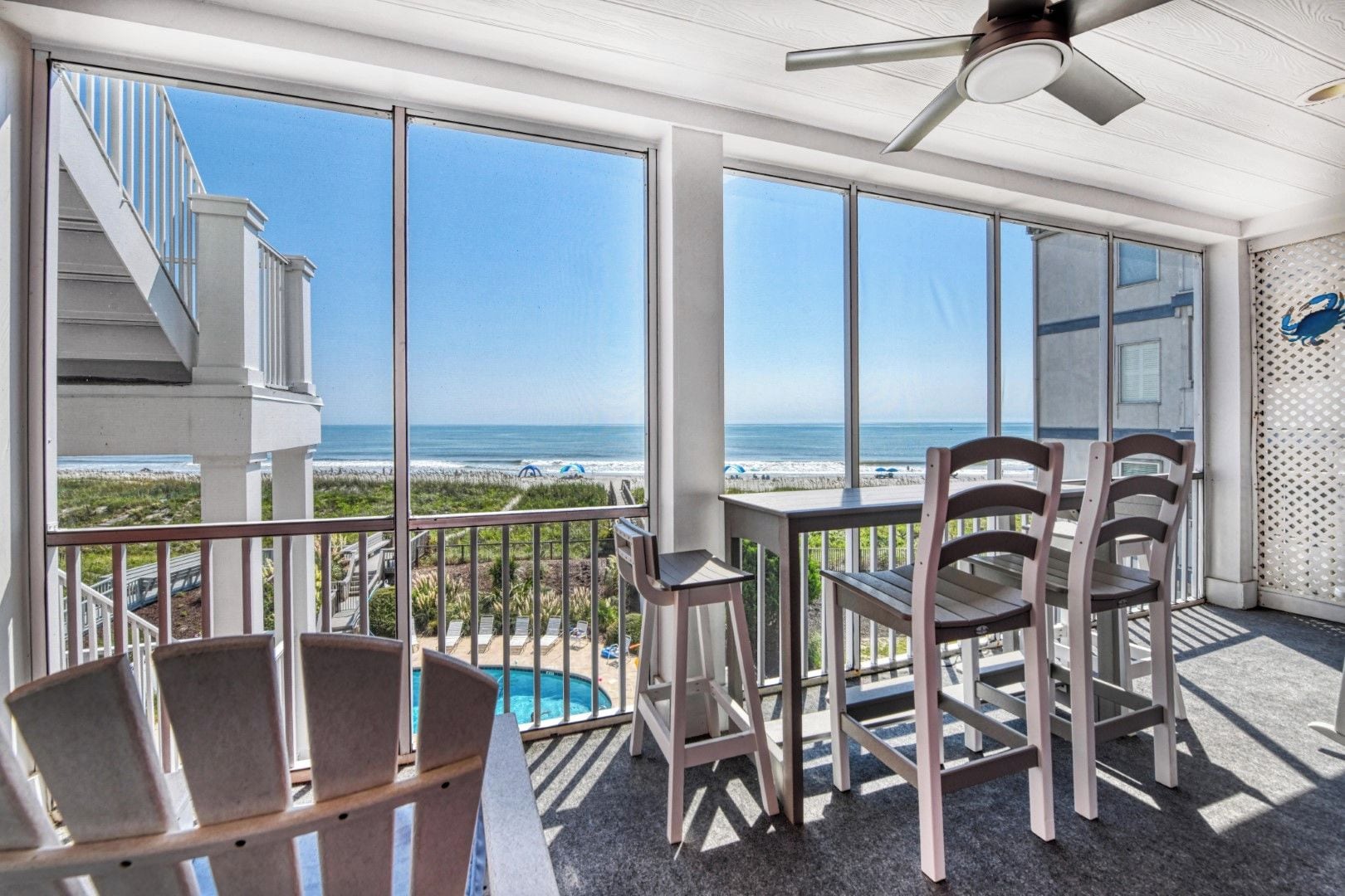 A balcony with a view of the beach, a pool, and a ceiling fan.