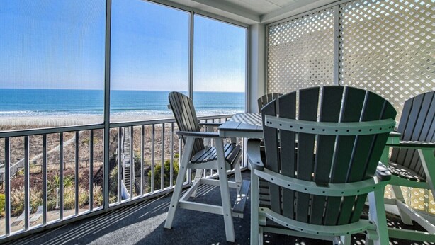 Ein überdachter Patio mit Blick auf den Strand, einem Tisch und Stühlen.
