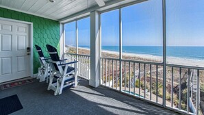 Ein überdachter Balkon mit Blick auf den Strand, eine weiße Tür und zwei Adirondack-Stühle.