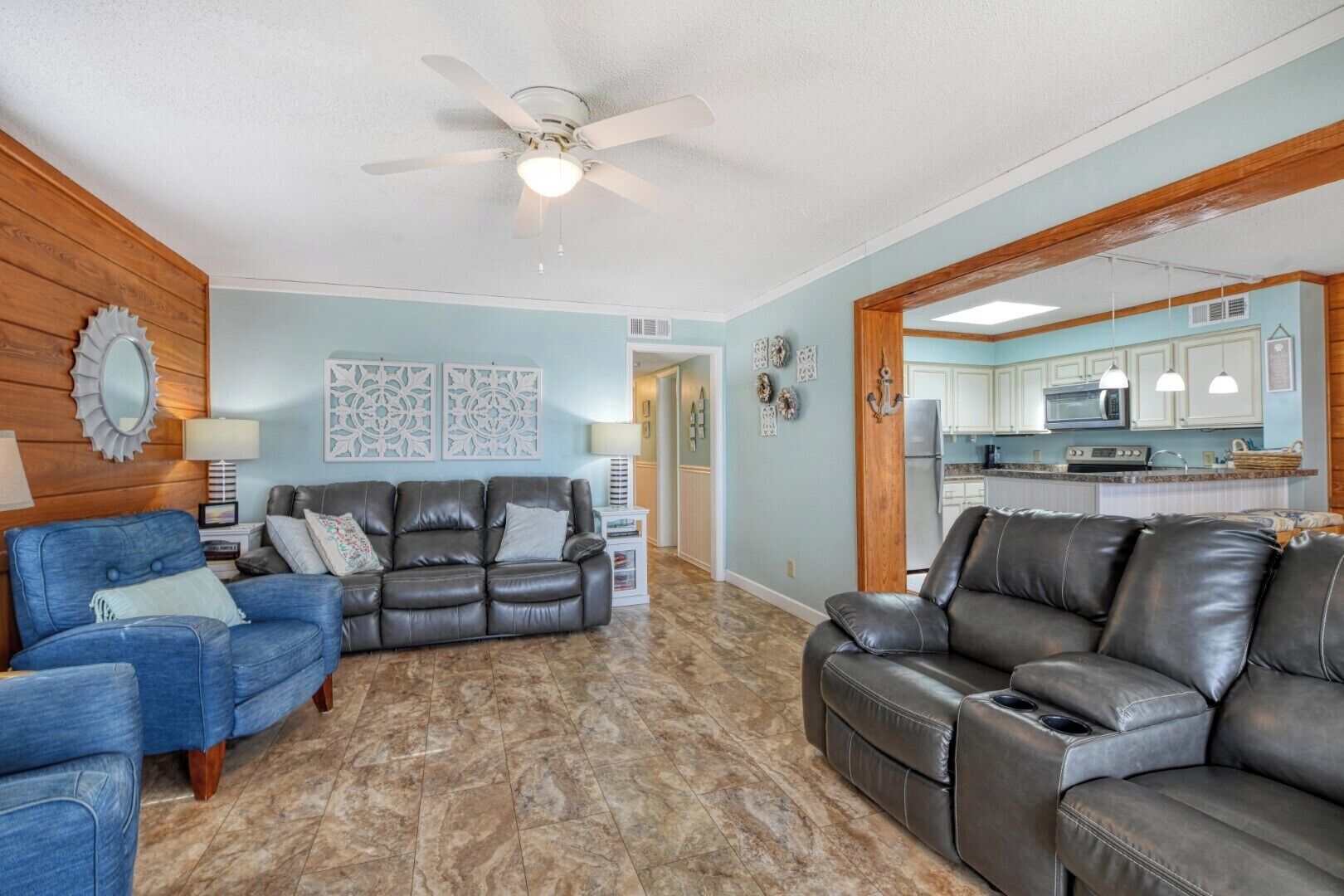 A living room with two leather sofas, a blue armchair, and a ceiling fan.