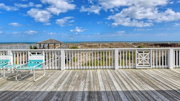Une terrasse en bois avec une balustrade blanche, un belvédère et une vue sur la plage.