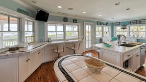Une cuisine avec des meubles blancs, un pare-feu en carreaux, une grande fenêtre et une vue sur l’extérieur.