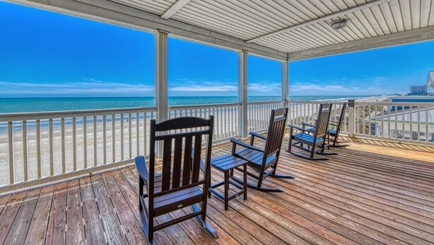 A covered deck with wooden flooring and metal railings, overlooking a beach and ocean. - Doctor's RX - Six Bedroom, Six Bath, Oceanfront Duplex with Private Pool (Myrtle Beach)