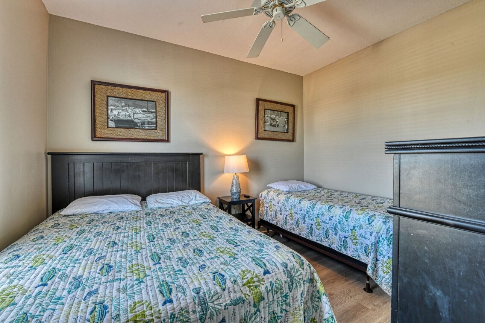 Une chambre d’hôtel avec deux lits, un ventilateur de plafond, une table de chevet avec une lampe et un réfrigérateur.