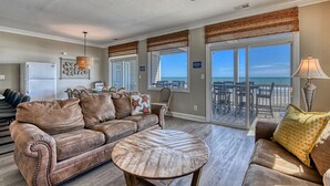 A spacious living room with a large brown leather sofa, a round coffee table, and a ceiling fan. There are large windows with a view of the ocean and a balcony with outdoor seating. - Doctor's RX - Six Bedroom, Six Bath, Oceanfront Duplex with Private Pool (Myrtle Beach)
