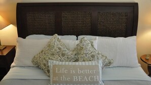 A neatly made bed with a decorative pillow and a sign stating "Life is better at the BEACH".