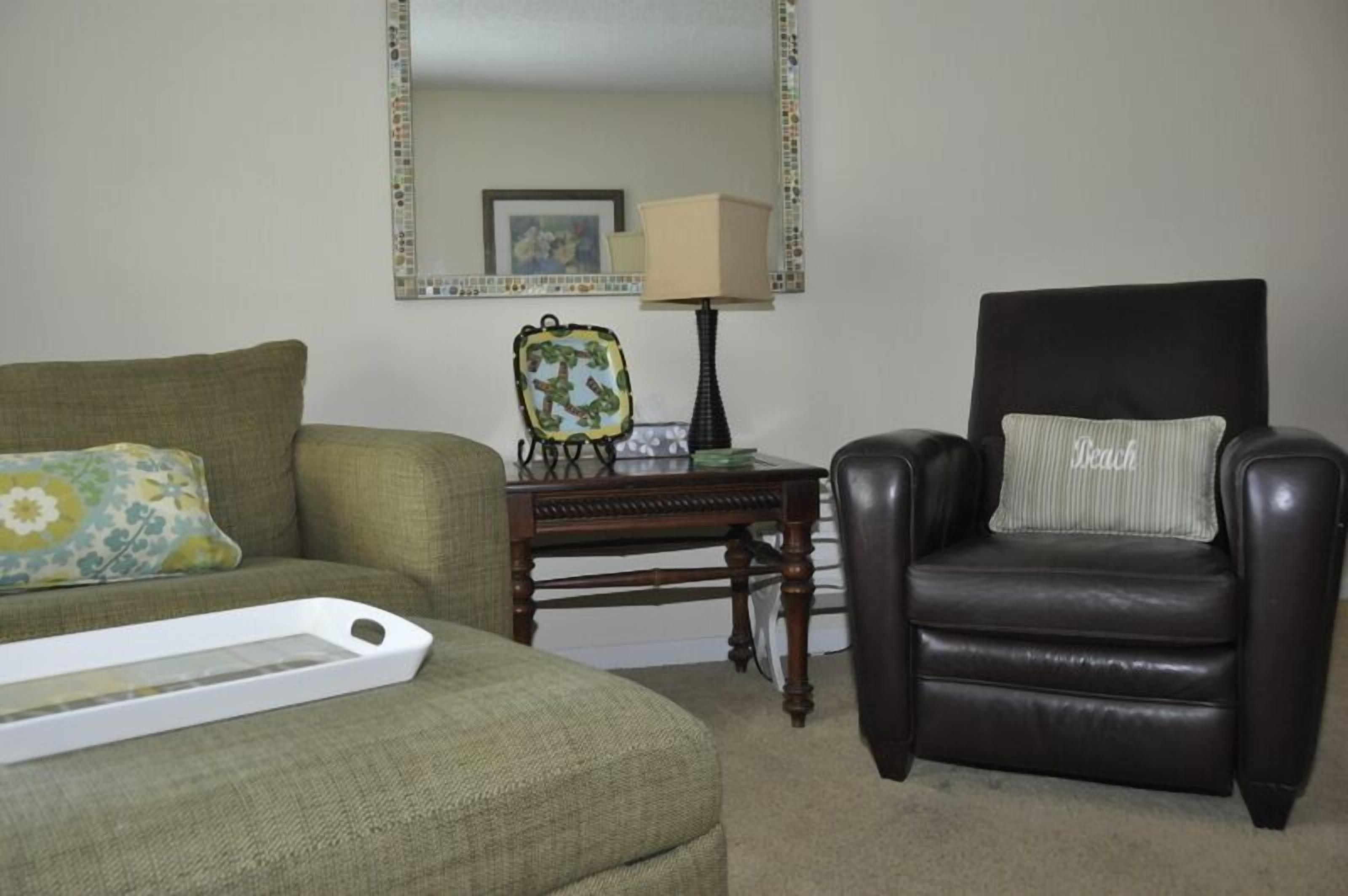 A living room with a green sofa, a black leather chair, a small wooden table, and a mirror on the wall.