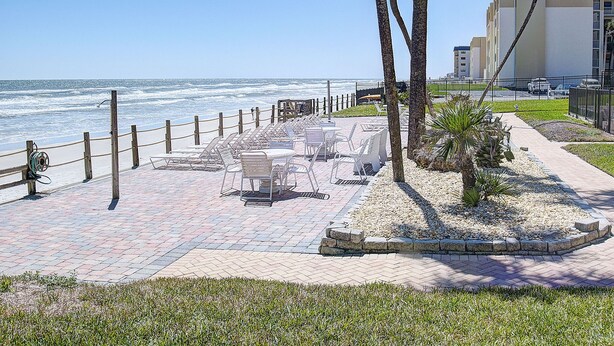 A seaside patio with outdoor seating, palm trees, and a view of the ocean.