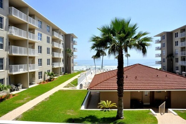 Un hôtel situé en bord de mer, doté de nombreux balcons, d’un palmier et offrant une vue dégagée sur l’océan.