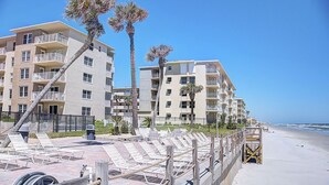 A beachfront hotel with multiple balconies, palm trees, and a sandy beach.