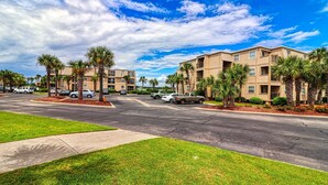 A multi-story residential building with a parking lot, surrounded by palm trees and a clear sky. - Inlet Pointe 30 Inlet front condo with pool, fishing dock and Walk to beach (Garden City Beach)