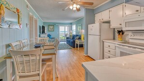 A spacious living area with a dining table, chairs, a sofa, and a kitchen with white cabinets and appliances. - Inlet Pointe 33, two-bedroom, two-bath Inlet/channel-front condo (Garden City Beach)