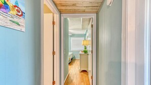 A narrow hallway with wooden flooring, light blue walls, and white trim. A door on the left leads to another room, and a small table with a lamp is visible in the distance. - Inlet Pointe 33, two-bedroom, two-bath Inlet/channel-front condo (Garden City Beach)