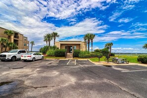 A parking lot with two cars, a building with a door, palm trees, and a picnic area. - Inlet Pointe 33, two-bedroom, two-bath Inlet/channel-front condo (Garden City Beach)