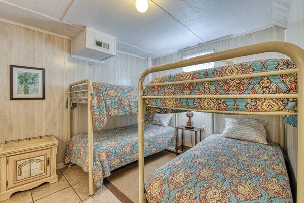 A bunk bed room with patterned bedding, a small cabinet, and a framed picture on the wall.