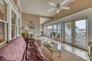 A spacious living room with a large window, a ceiling fan, and a cozy seating area with a sofa and chairs.