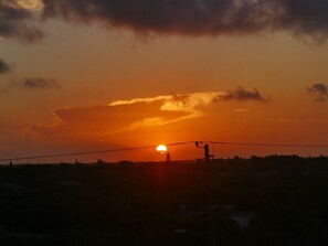 Un atardecer sobre un paisaje con una línea eléctrica y un poste de servicios en primer plano.