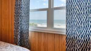 Une pièce avec un mur lambrissé en bois, une fenêtre donnant sur la plage et des rideaux à motifs.
