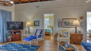 A spacious living room with a television, seating area, and a bed in the background. - Lazy O - Four Bedroom, Three 1/2 Bath Oceanfront Home with Private Pool (Garden City Beach)
