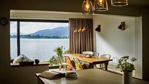 Un coin repas avec vue sur un lac et des montagnes, une table avec des chaises et une fenêtre avec des rideaux.