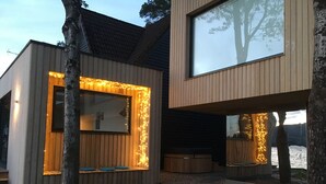Une maison moderne dotée d’une grande fenêtre, d’une terrasse en bois et d’un chemin en pierre.