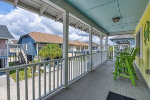 Eine überdachte Veranda mit Geländer, grünen Stühlen und Blick auf die Nachbarhäuser.