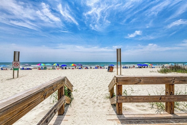 Ein Strand mit Holzstegen, Sonnenschirmen und einem Verbotsschild für Feuerwerkskörper.