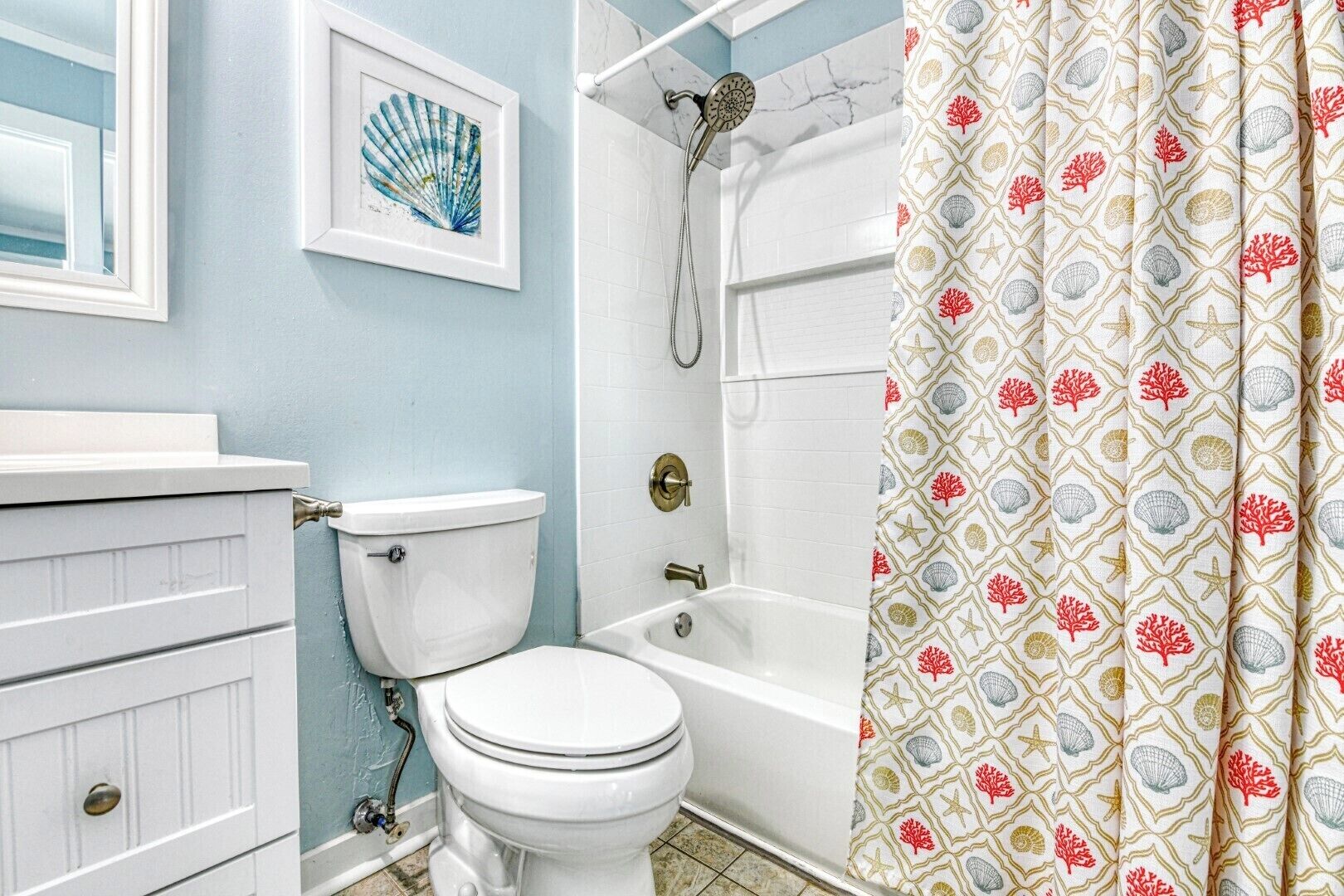 Un baño con inodoro, bañera, ducha y cortina con estampado de conchas.