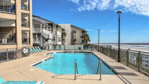 A pool area with lounge chairs, a lifeguard stand, and a view of the ocean.