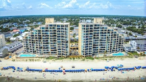 A beachfront hotel with multiple high-rise buildings, a sandy beach, and a pool area.
